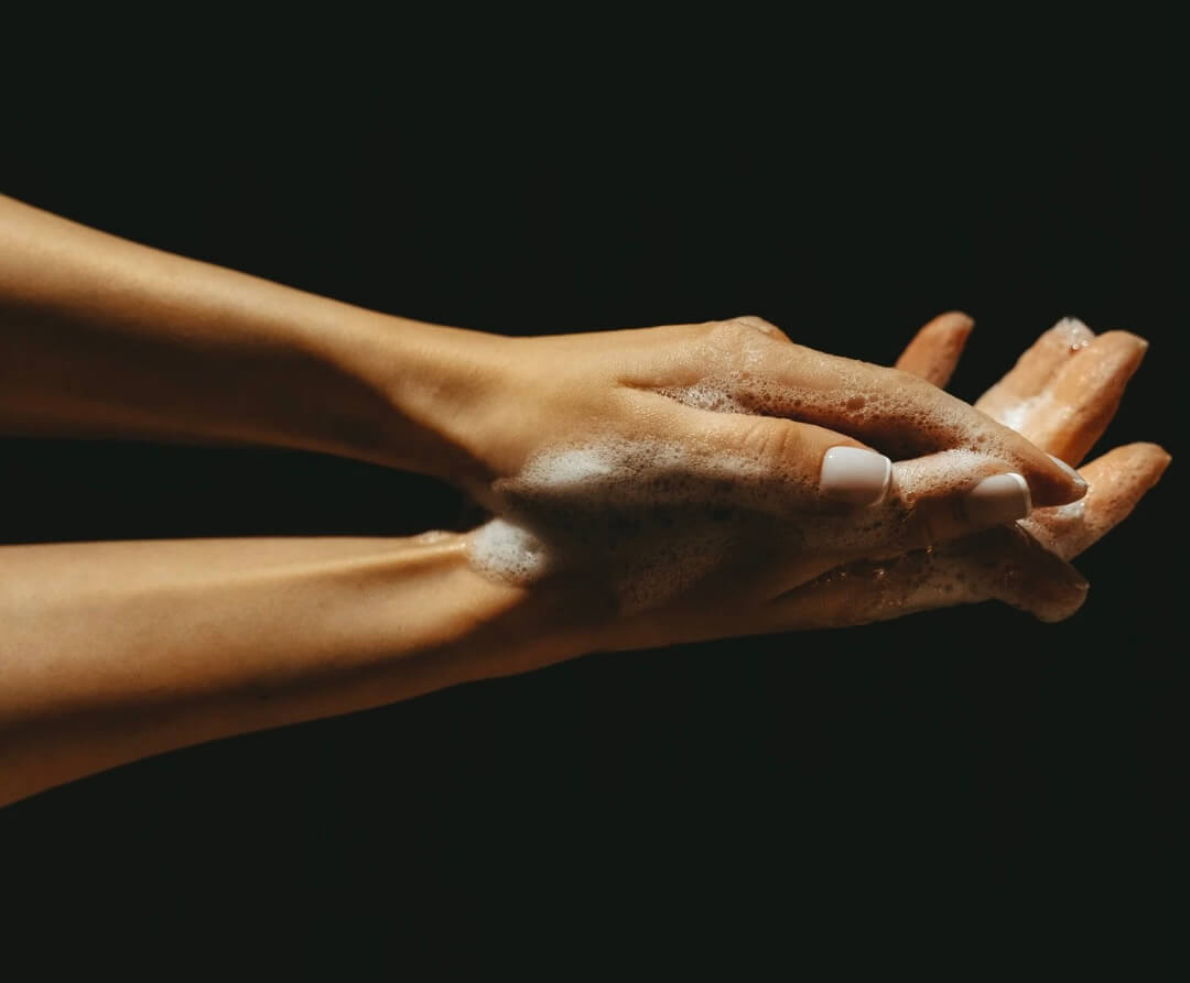 Two hands above each other covered with bubbles and foam in front of black background