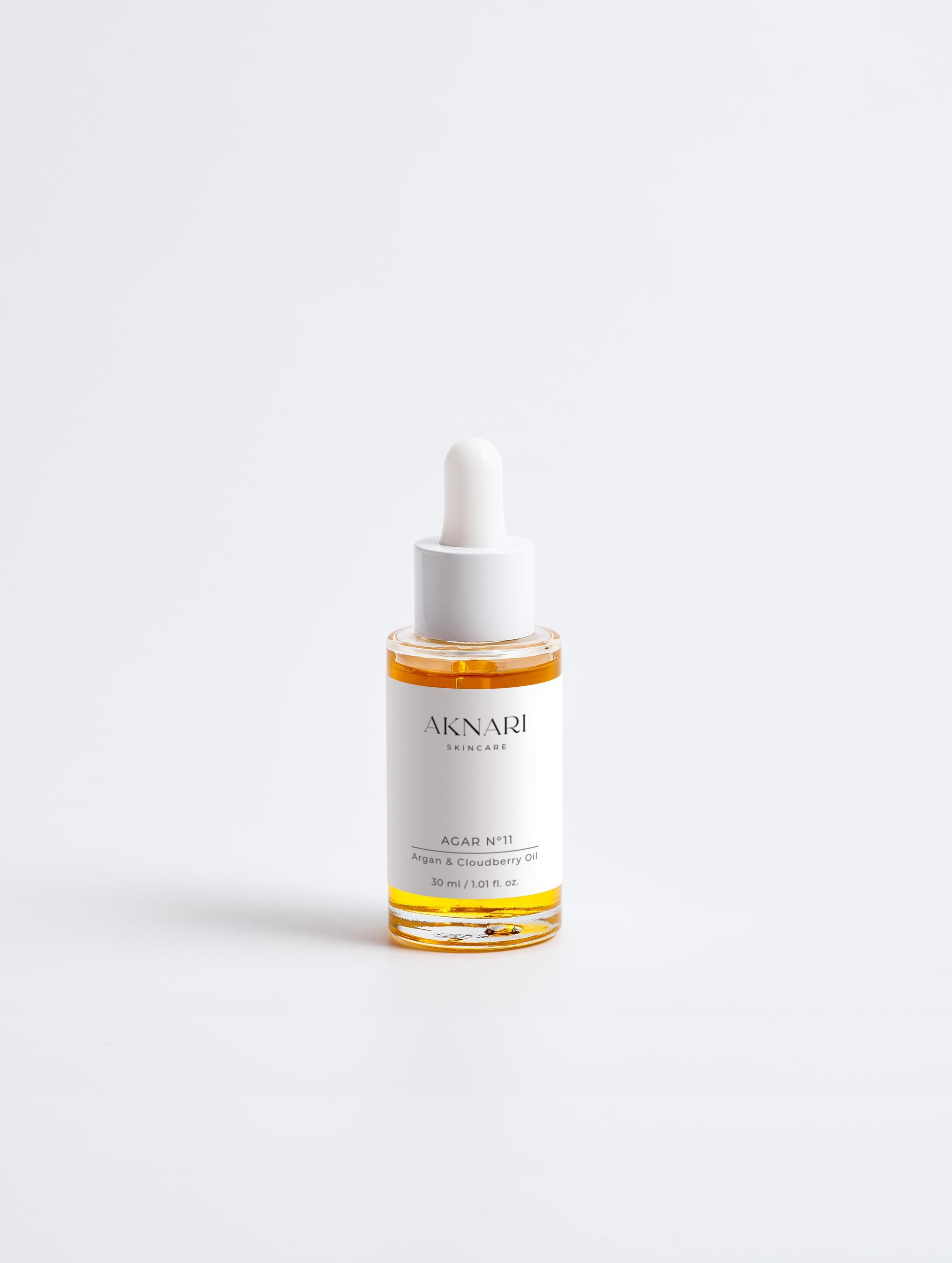 Glass pump bottle with white label and oil inside in front of white background
