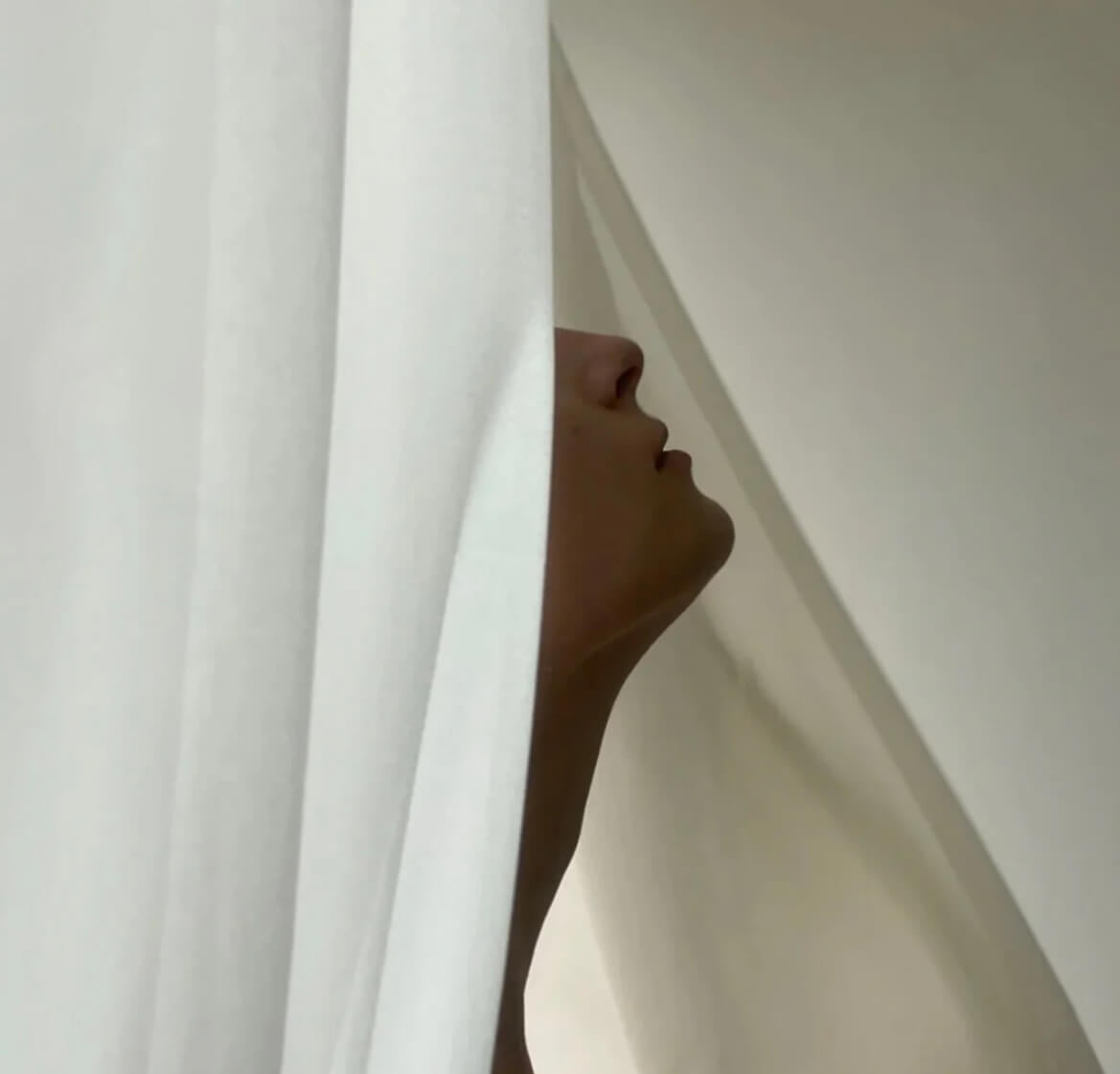 White sheets and a chin, lips and nose of a woman showing in the middle of the sheets.