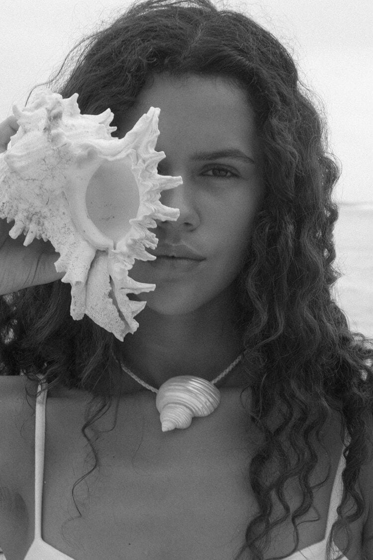 Woman with curly hair is holding a sea shell close to her face.