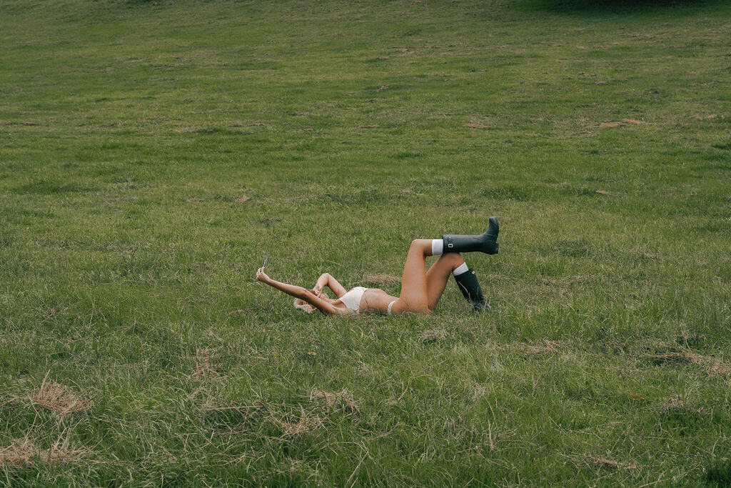 Woman laying in grass wearing white underwear and rain boots.